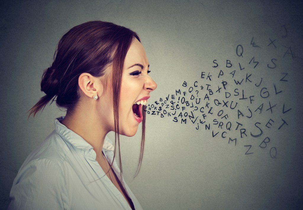 Side profile angry woman screaming with alphabet letters flying out of wide open mouth isolated on gray wall background