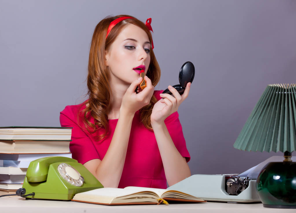 Woman at typewriter applying lipstick.