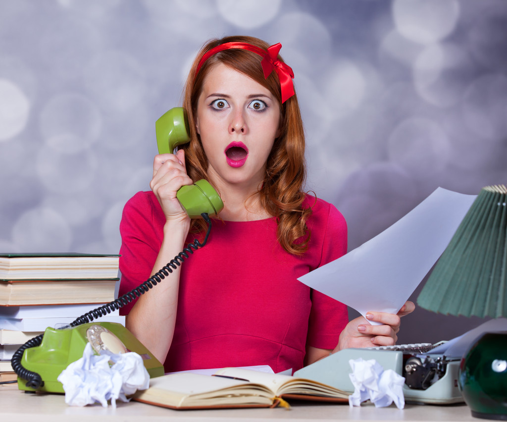 Woman at typewriter on telephone with surprised expression on face.