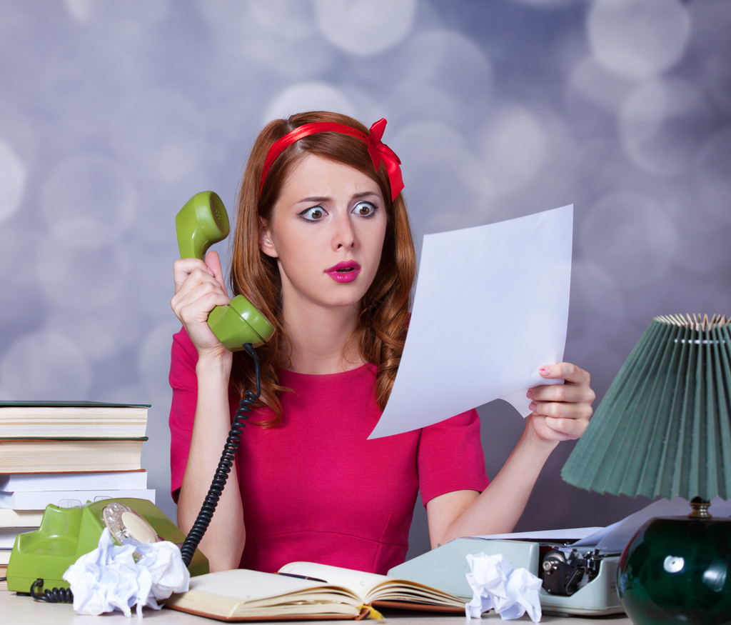 Woman at typewriter holding telephone.