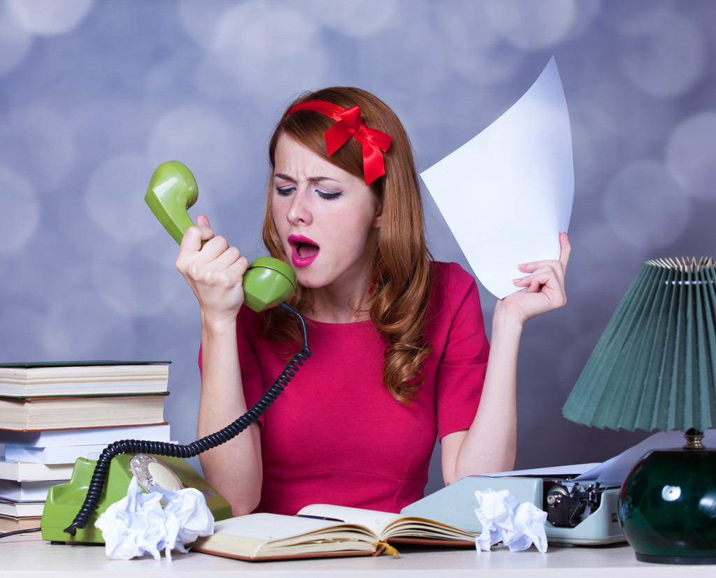 Woman at typewriter shouting at telephone.